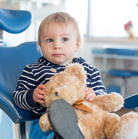 young boy sitting in a dental chair with his teddy bear