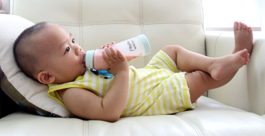 Baby relaxes on the couch as he drinks from a bottle