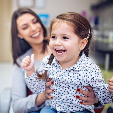 young, smiling girl being held by her mother while at a dentist's office